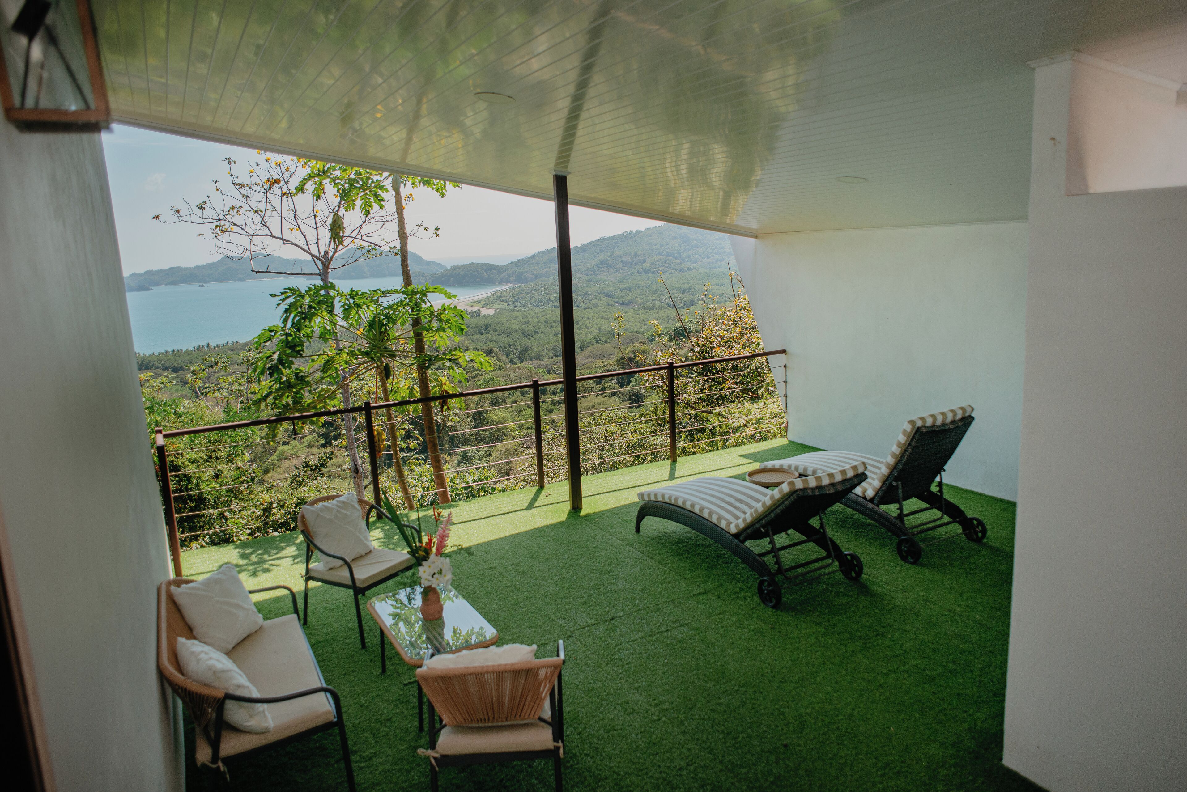 A balcony with a view of a lake and mountains, furnished with chairs and a table.