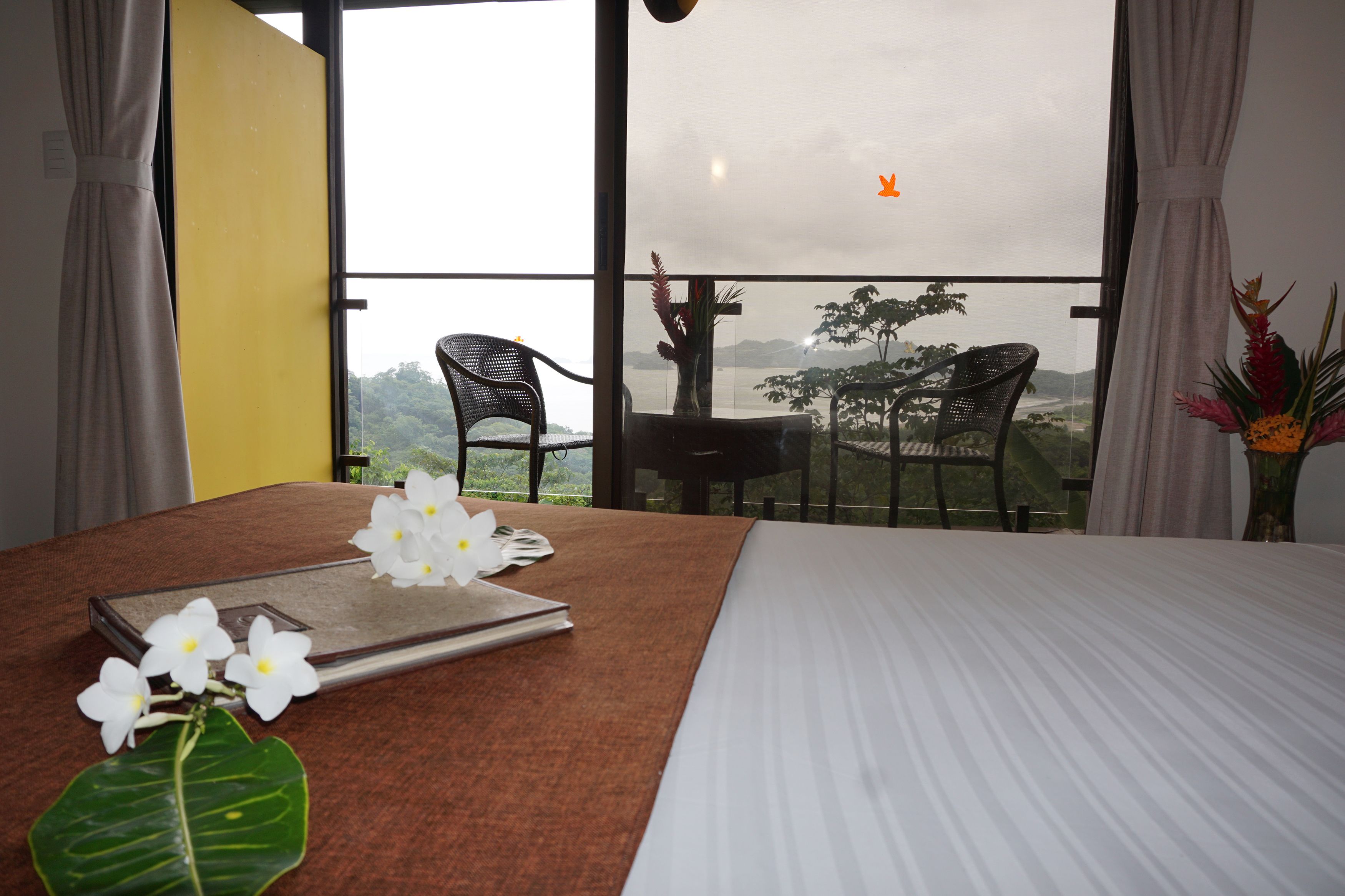 A hotel room with a bed, a table with chairs, and a view of the outdoors.
