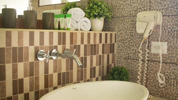A bathroom with a white sink, a mirror, a hairdryer, and a potted plant.