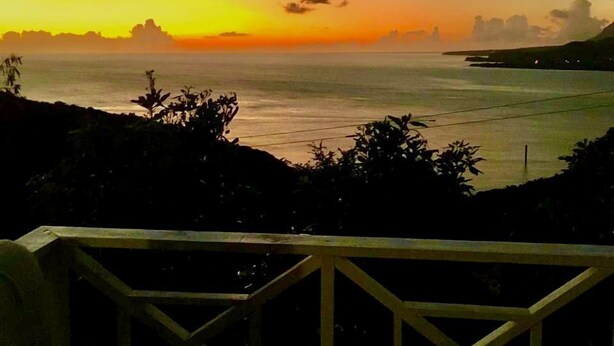 Vista del atardecer en la costa, con una barandilla de madera al frente.
