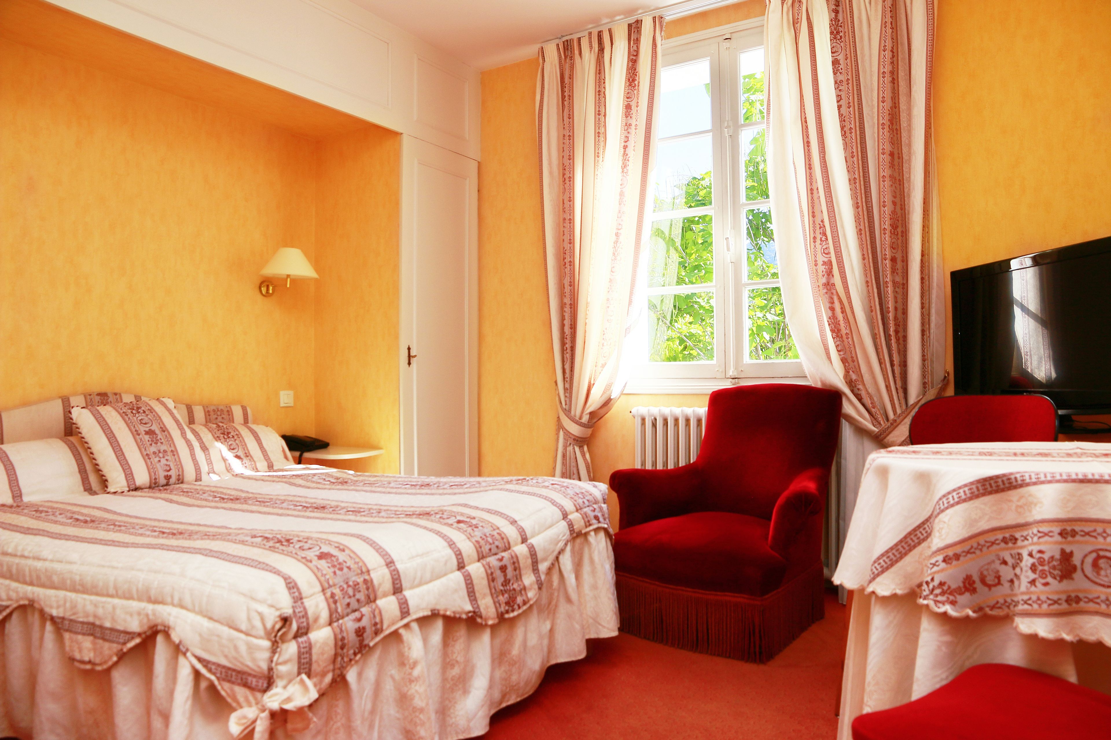 A hotel room with two beds, a red armchair, a table with a white tablecloth, and a TV.