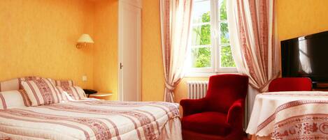 A hotel room with two beds, a red armchair, a table with a white tablecloth, and a TV.
