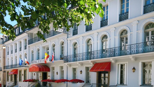 Hotel histórico con toldo rojo, mesas al aire libre y banderas.
