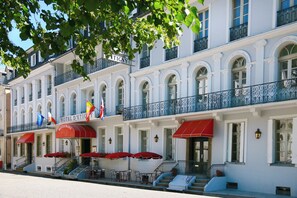 Hotel histórico con toldo rojo, mesas al aire libre y banderas.
