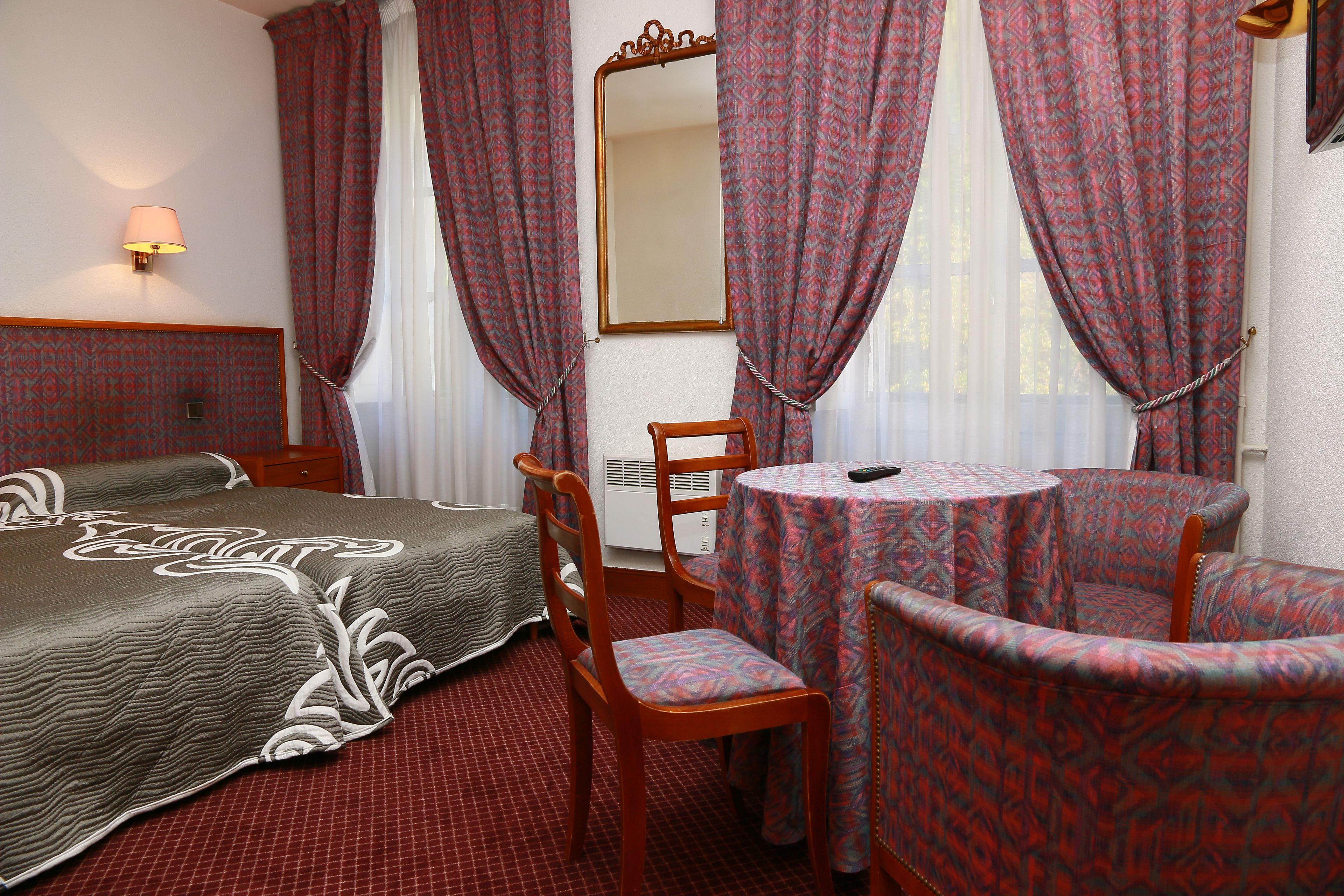 Una camera d'albergo con un letto, un tavolino rotondo, due sedie, uno specchio e tende a motivi.