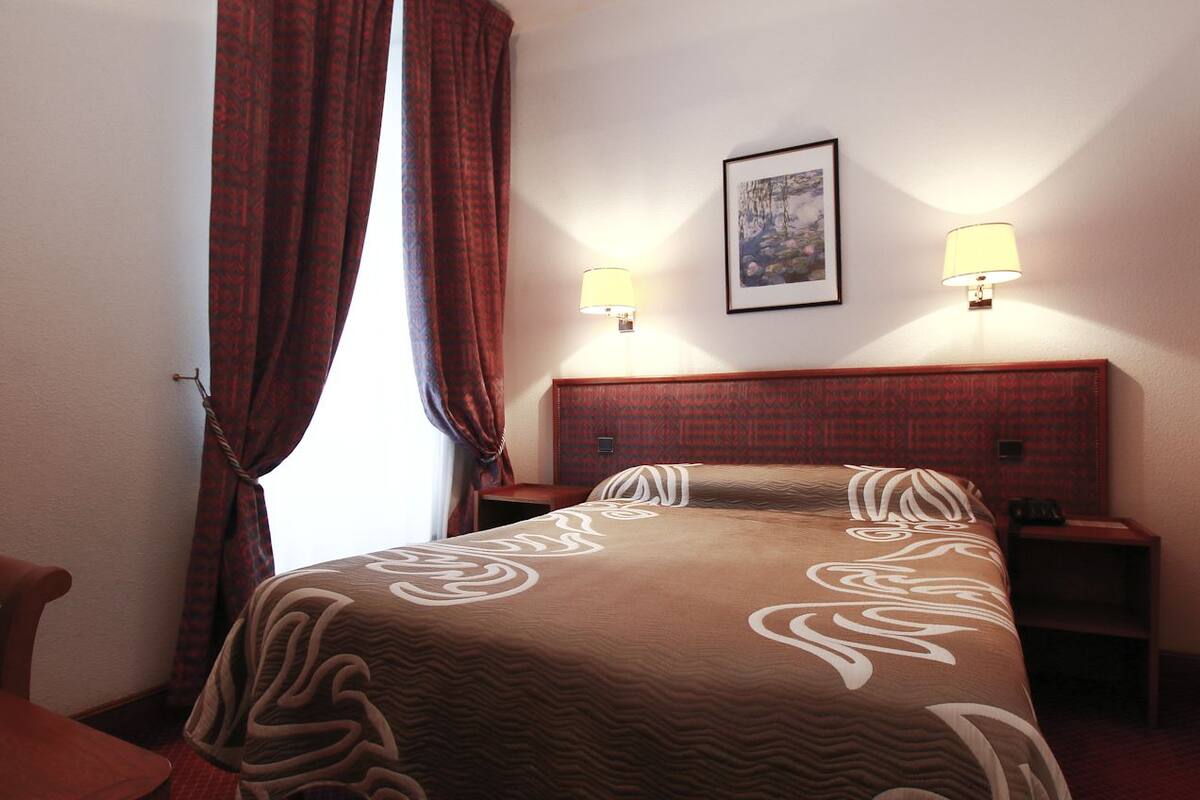 Habitación de hotel con una cama, dos lámparas de noche, un cuadro enmarcado en la pared y un cabecero de madera.