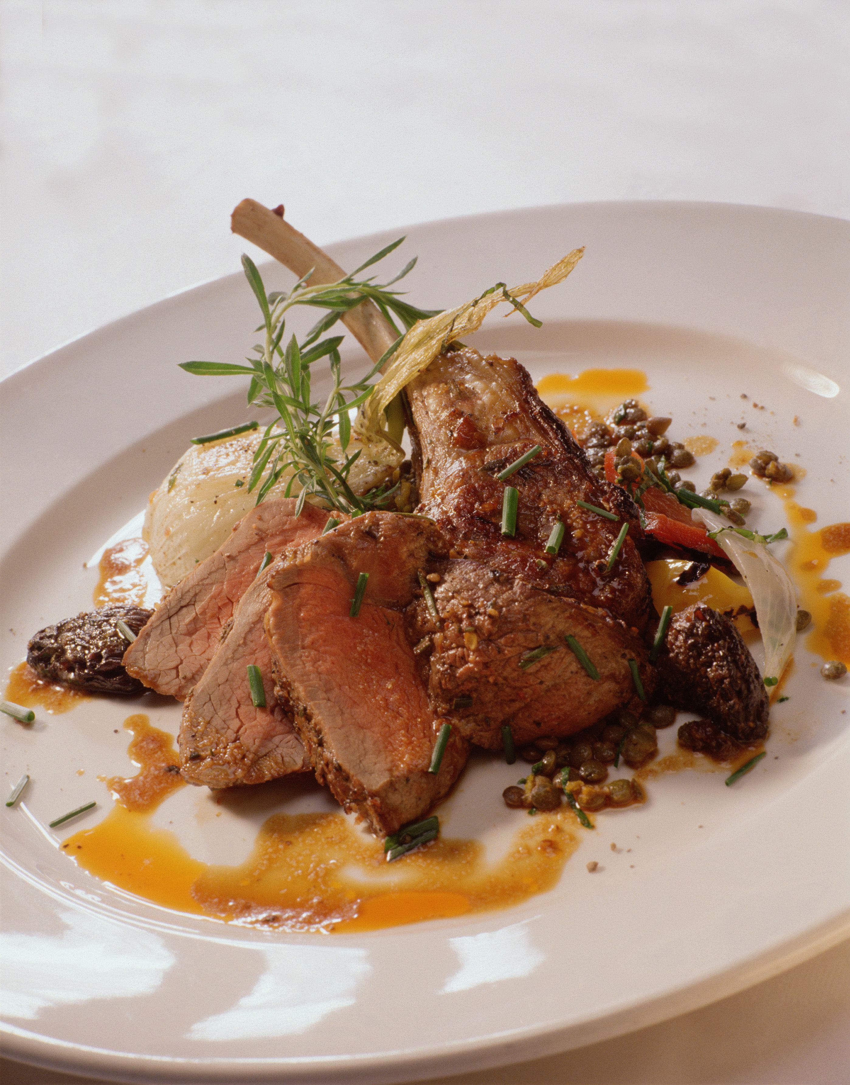 Une assiette contenant un morceau d’agneau, des légumes et une sauce.