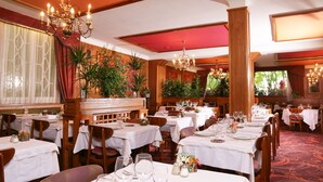 Un restaurante con varias mesas dispuestas para comer, con candelabros y plantas en macetas.