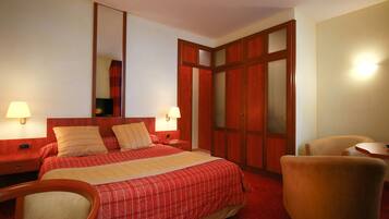A hotel room with a large bed, two bedside tables with lamps, a wooden wardrobe, and a single armchair.