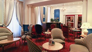 Un vestíbulo de hotel con alfombra roja, varias zonas de estar con tapicería estampada, un área de bar con una pared de acento azul y un candelabro.