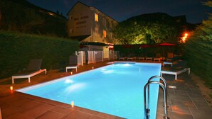 Una piscina con sillas de descanso y sombrillas, rodeada por un jardín ajardinado y un edificio con el letrero "Hotel D'Etigny Restaurant".