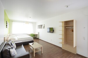 Una habitación moderna y bien iluminada con cama, sofá, televisor y armario de madera.
