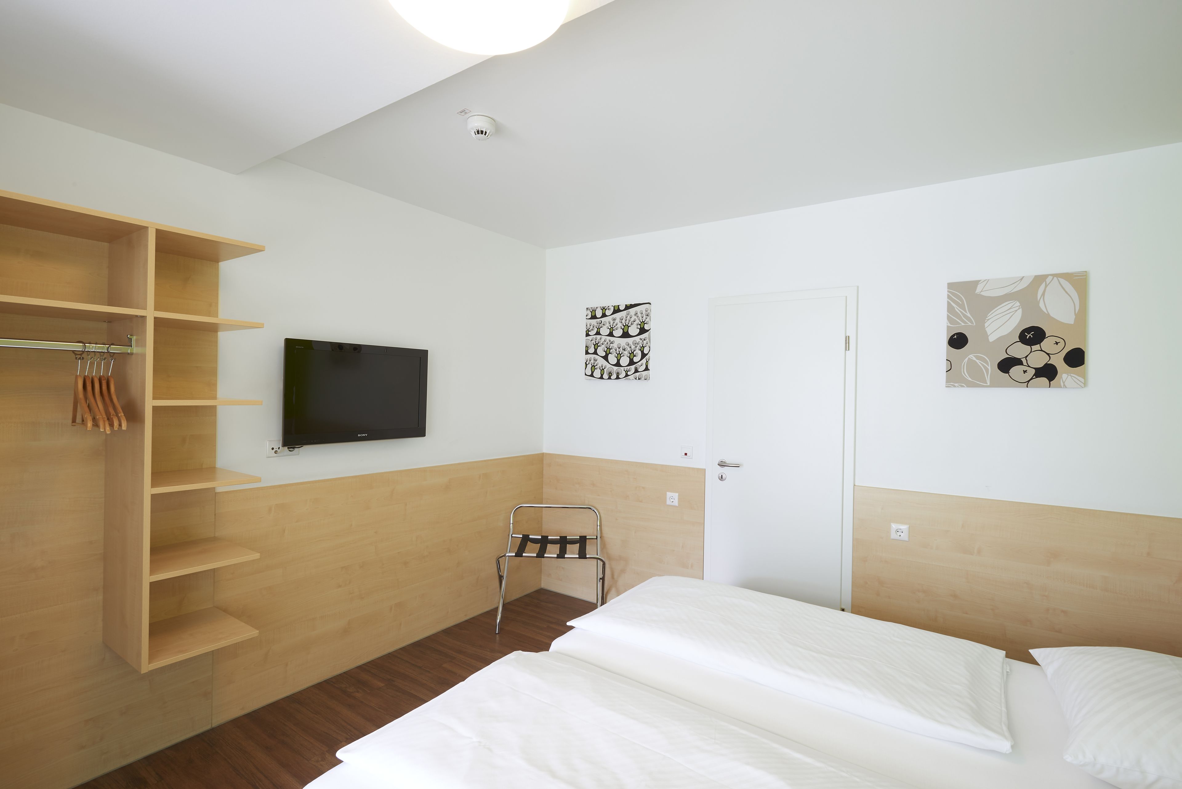 A hotel room with a bed, a TV, a wardrobe, and artwork on the walls.