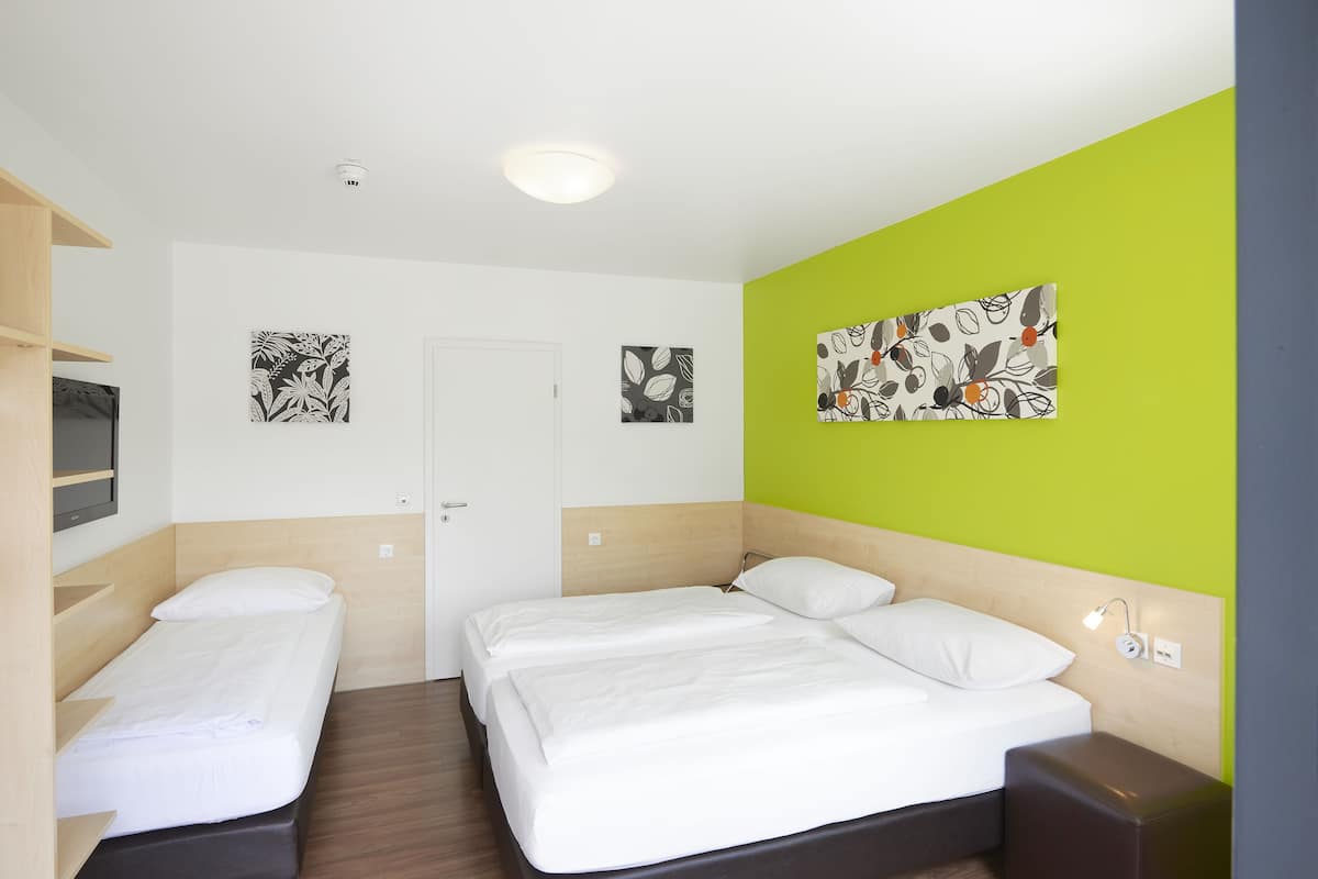 A hotel room with two single beds, a wooden headboard, a green accent wall, and artwork on the walls.