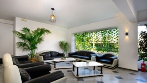 A modern living room with black and white sofas, a coffee table, and a large potted plant. - Aquarius Beach Eco-Hotel (Corfu)