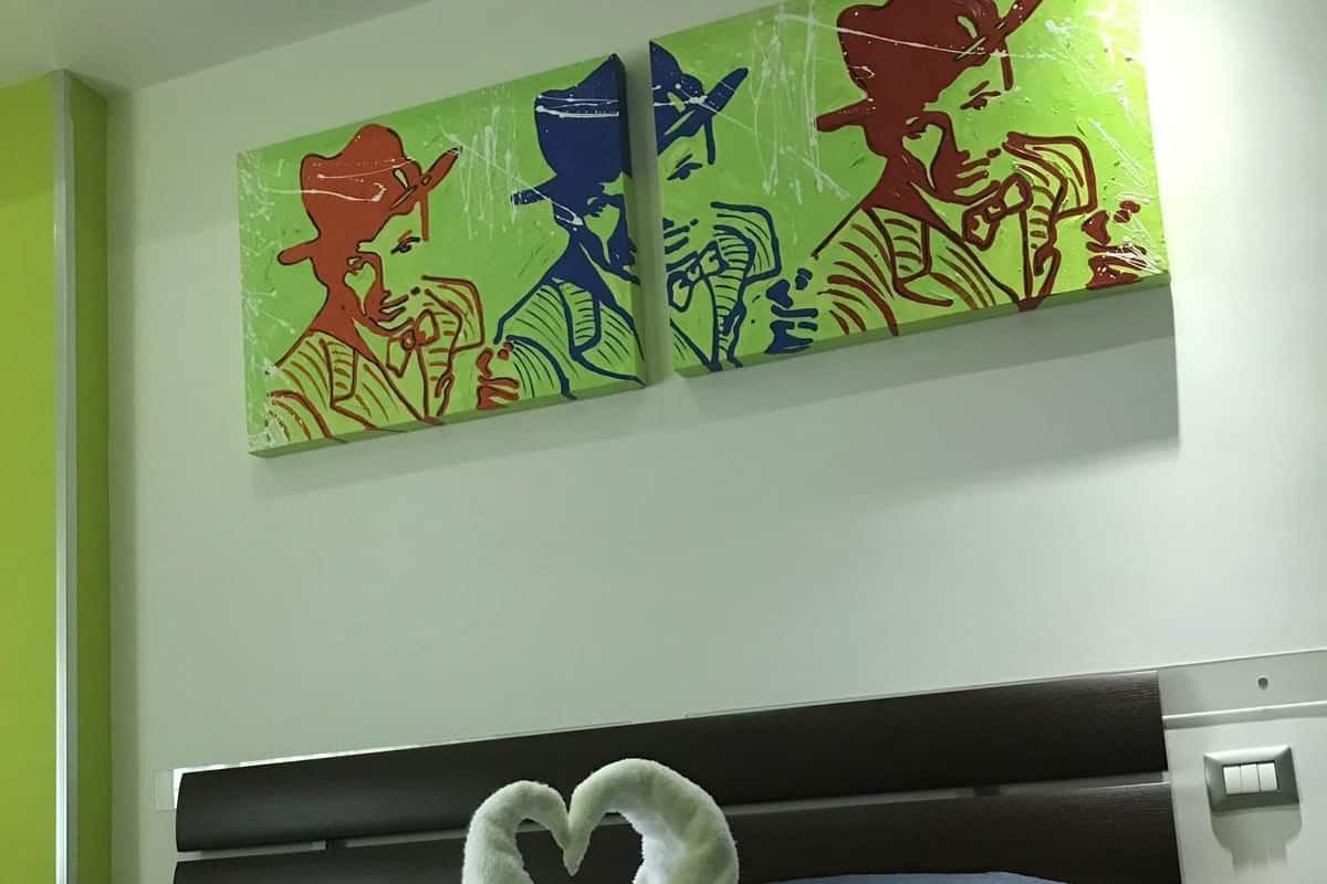 A bed with a heart-shaped towel arrangement and two colorful paintings on the wall.