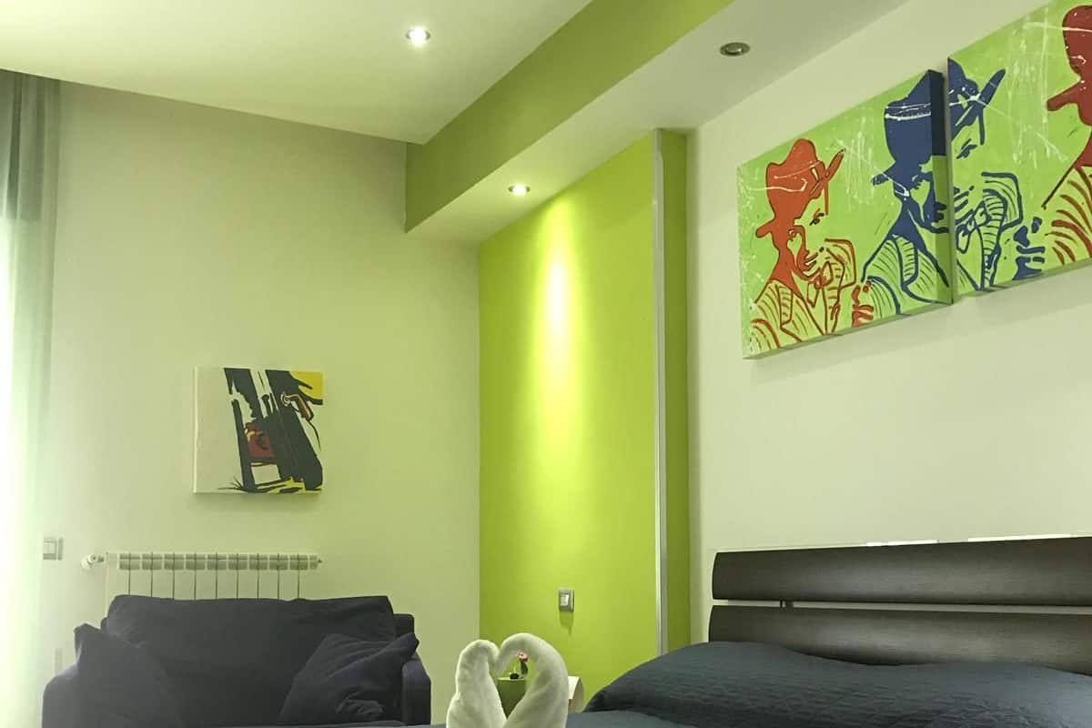 A hotel room with a large bed, a green accent wall, and a painting on the wall.