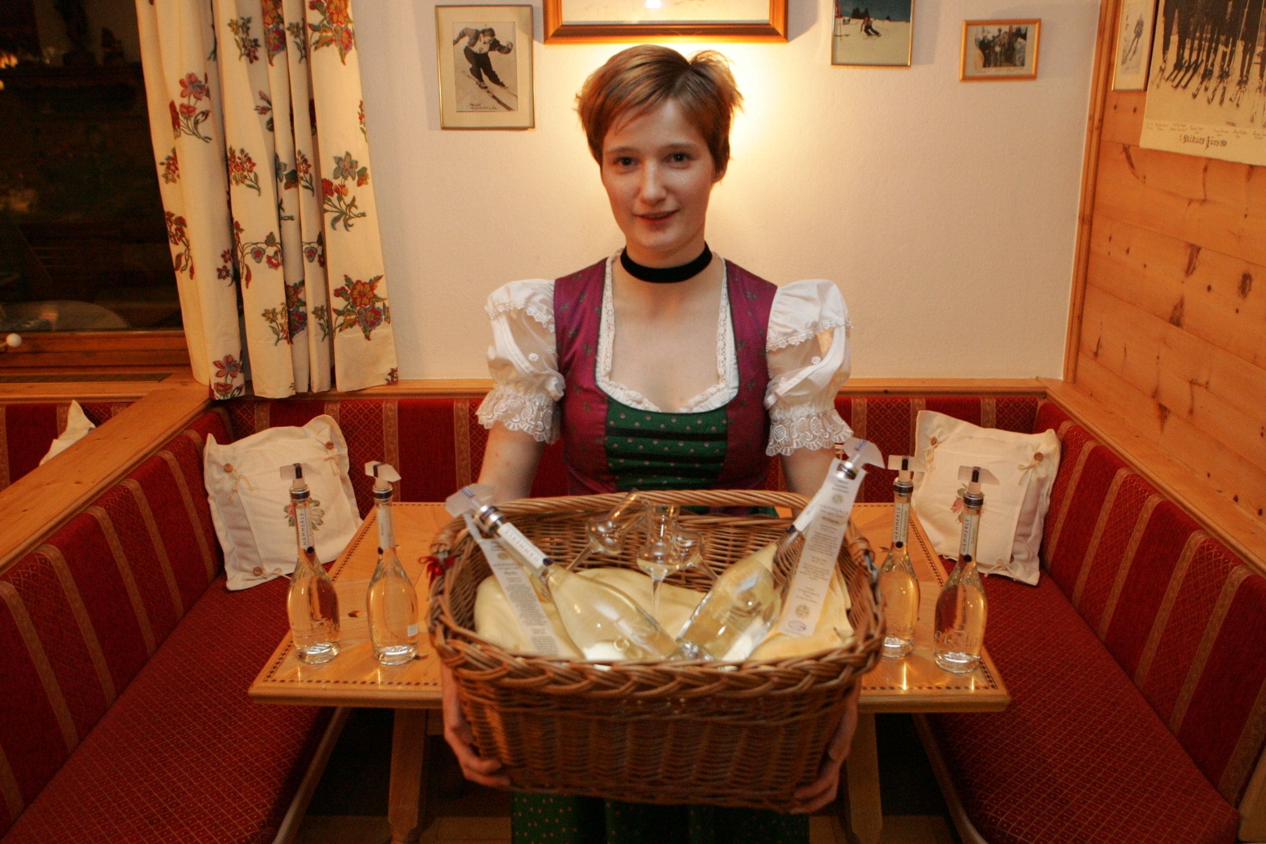 A person seated at a table with a basket of bottles and glasses.