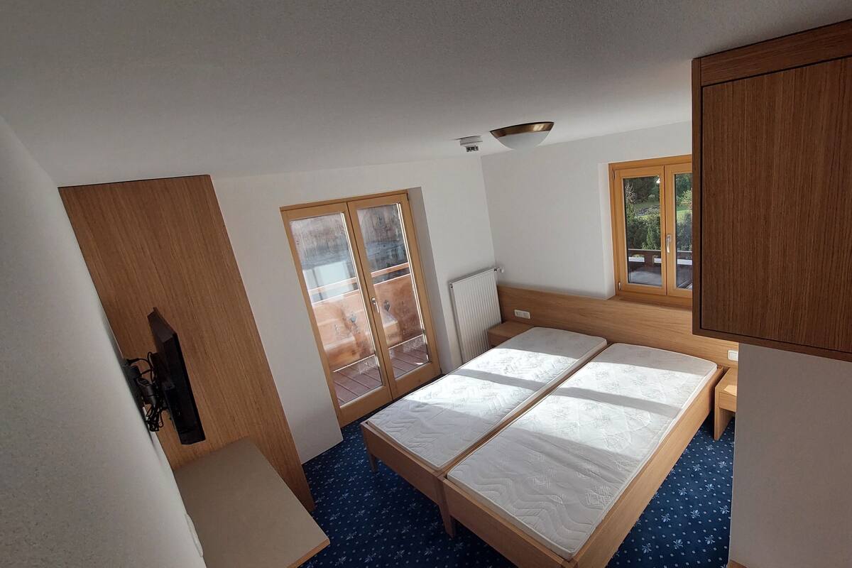 Una habitación pequeña y luminosa con una cama, un ventanal y un radiador.