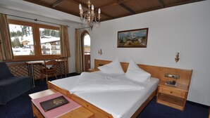 Una camera d'albergo con un letto in legno, una scrivania con una sedia, un tavolino con un libro e un quadro appeso al muro.