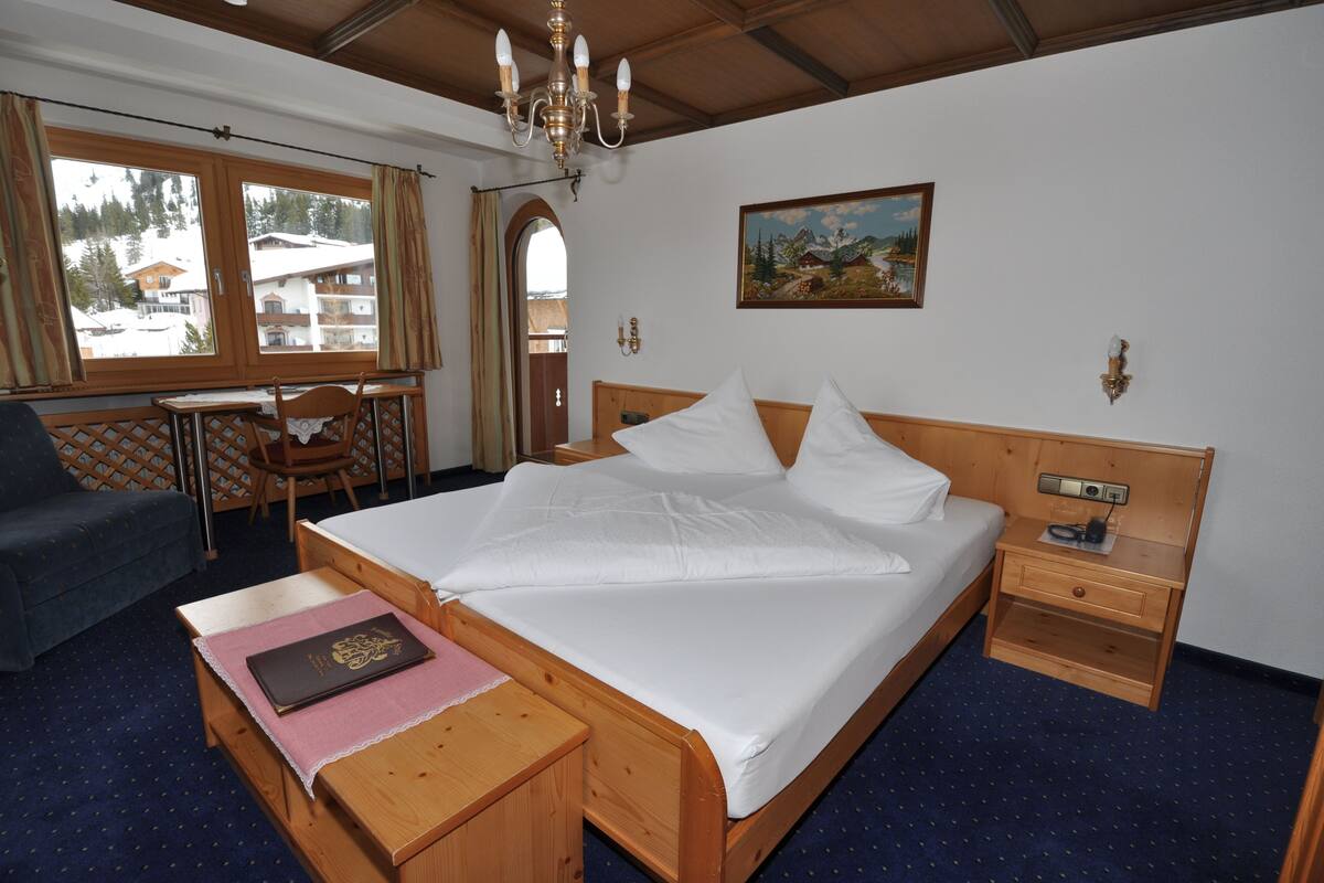 Una habitación de hotel con una cama de madera, un escritorio con una silla, una mesita con un libro y un cuadro en la pared.