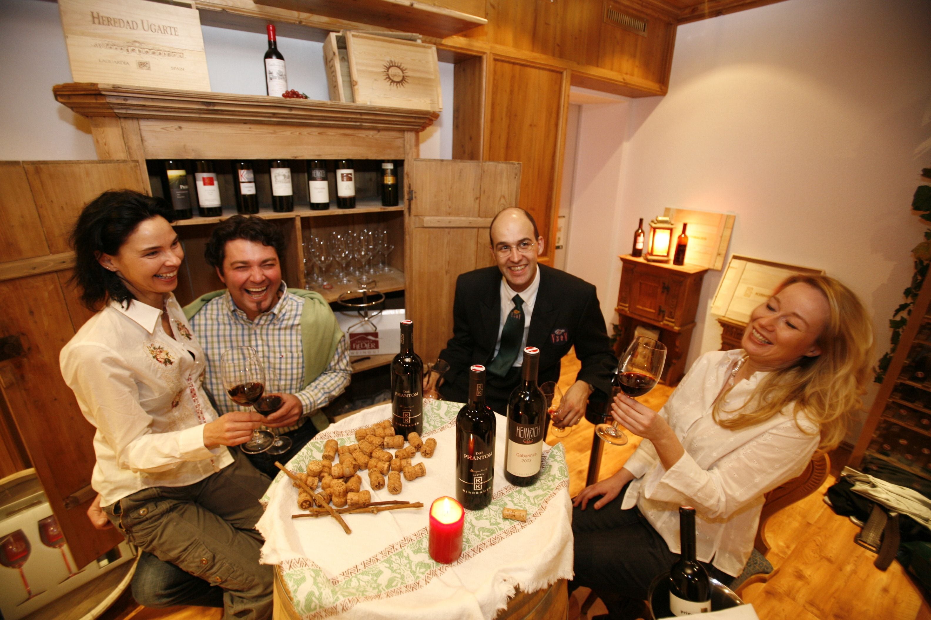 A group of people seated around a table with wine bottles and glasses, in a room with wooden walls and shelves of wine bottles.