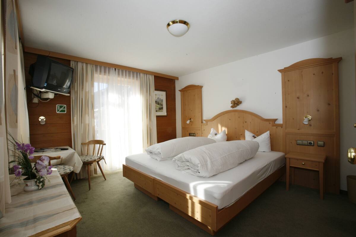 Un dormitorio con una cama de madera, un escritorio con silla, un televisor montado en la pared y un armario.