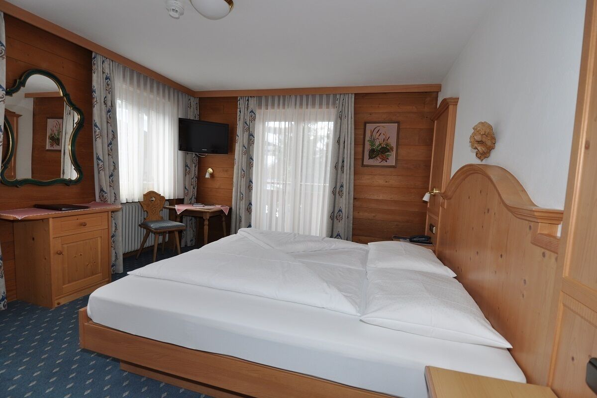 Una habitación de hotel con una cama de madera, un escritorio con una silla, un televisor y un espejo.