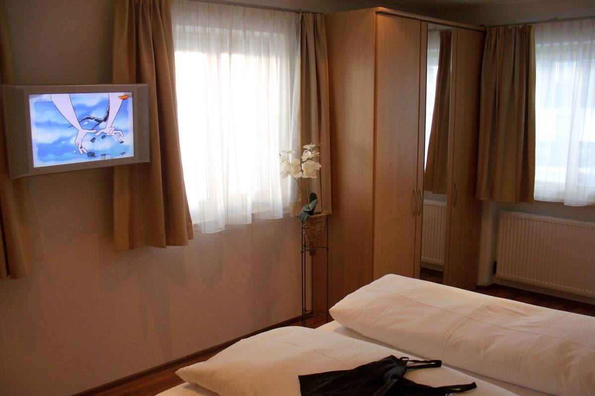 Habitación de hotel con dos camas, un televisor en la pared y una ventana con cortinas.