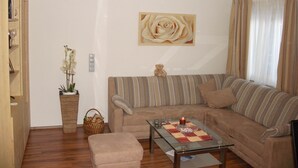 A living room with a sofa, a glass coffee table, a small table with a candle, a teddy bear, and a wall-mounted rose painting. - Hotel Stülzis (Lech am Arlberg)