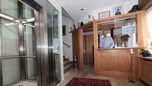 Una hall con una reception in legno, una scala e un ascensore in vetro.