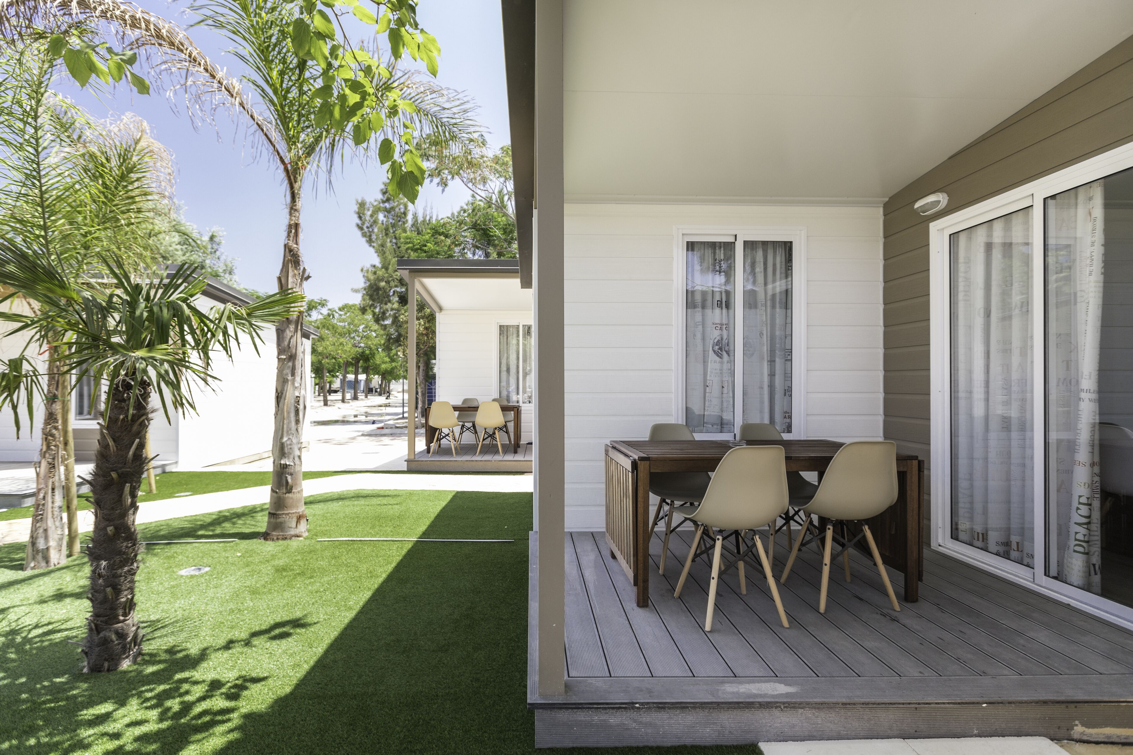 A patio with a wooden table and chairs, a small lawn, and palm trees.