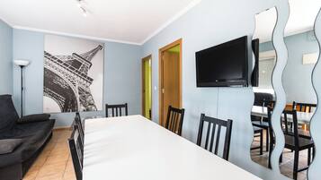 A modern room with a dining table, chairs, a sofa, a TV, and a wall with a large black and white picture.