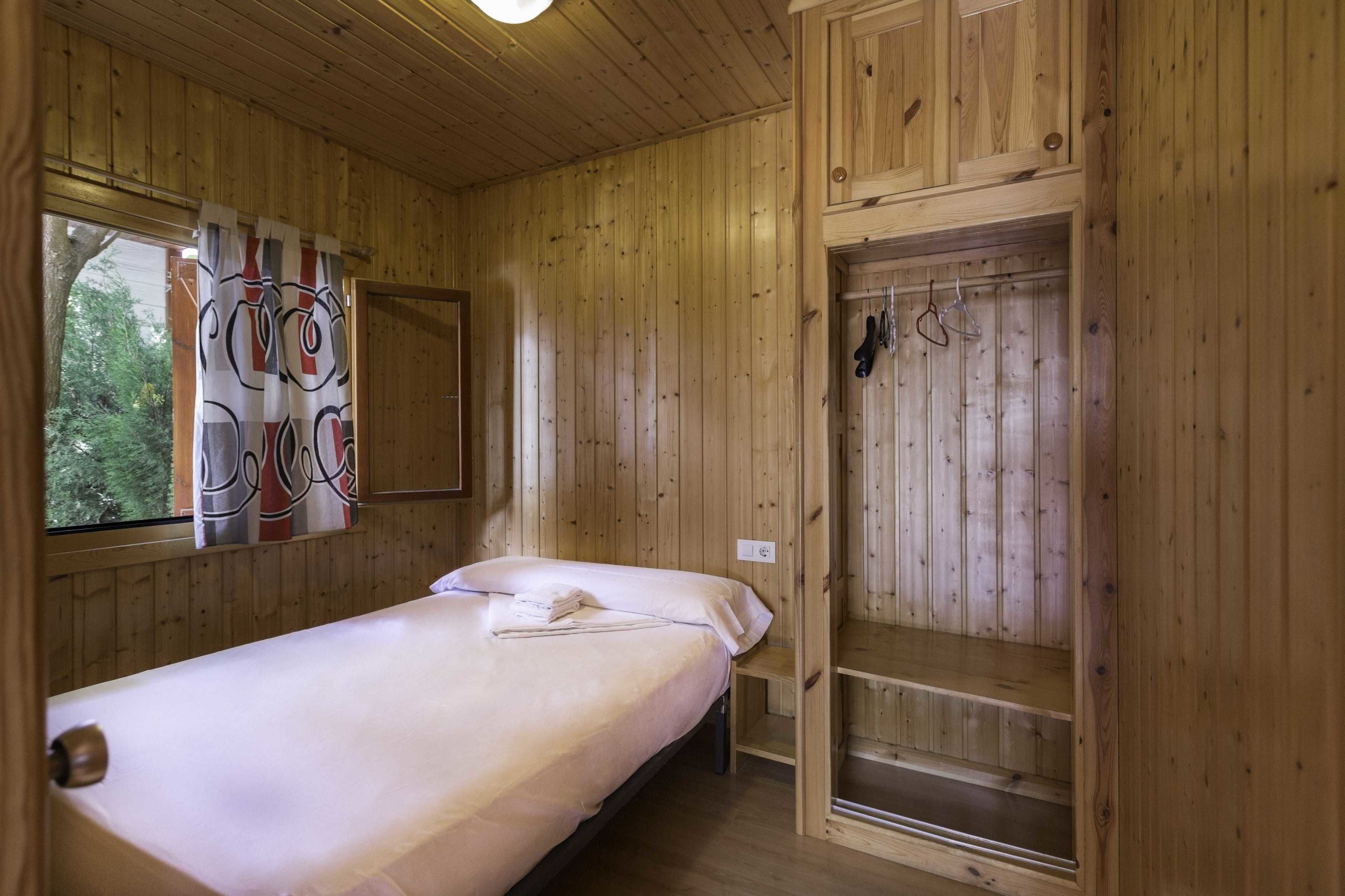 A wooden cabin room with a single bed, a small table, and a built-in wardrobe.