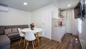 A compact living space with a dining area, kitchenette, and a flat-screen TV mounted on the wall. - Camping Los Llanos (Denia)