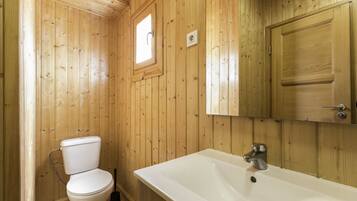 Une salle de bain aux murs lambrissés, équipée de toilettes, d’un lavabo et d’une fenêtre.