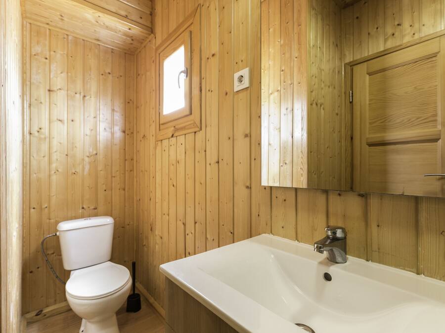 Un baño con paneles de madera, un inodoro, un lavabo y una ventana.