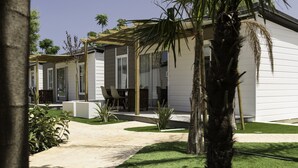 A modern house with a covered patio, a lawn, and a palm tree. - Camping Los Llanos (Denia)