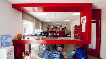 Un área de recepción con un escritorio rojo, un dispensador de agua y una vitrina de vidrio con varios objetos.