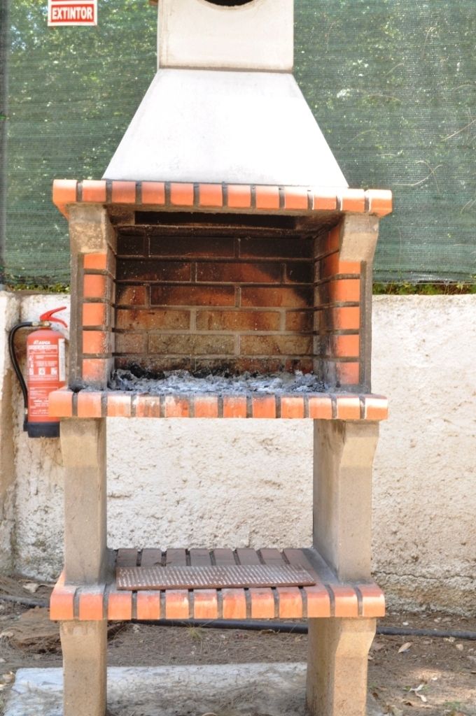 Un horno para pizza de ladrillo con chimenea, un extintor y una rejilla de metal.