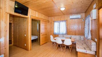 A wooden cabin with a dining area, a bed, and an air conditioning unit.