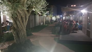 An outdoor dining area with tables and chairs, surrounded by buildings and a tree.