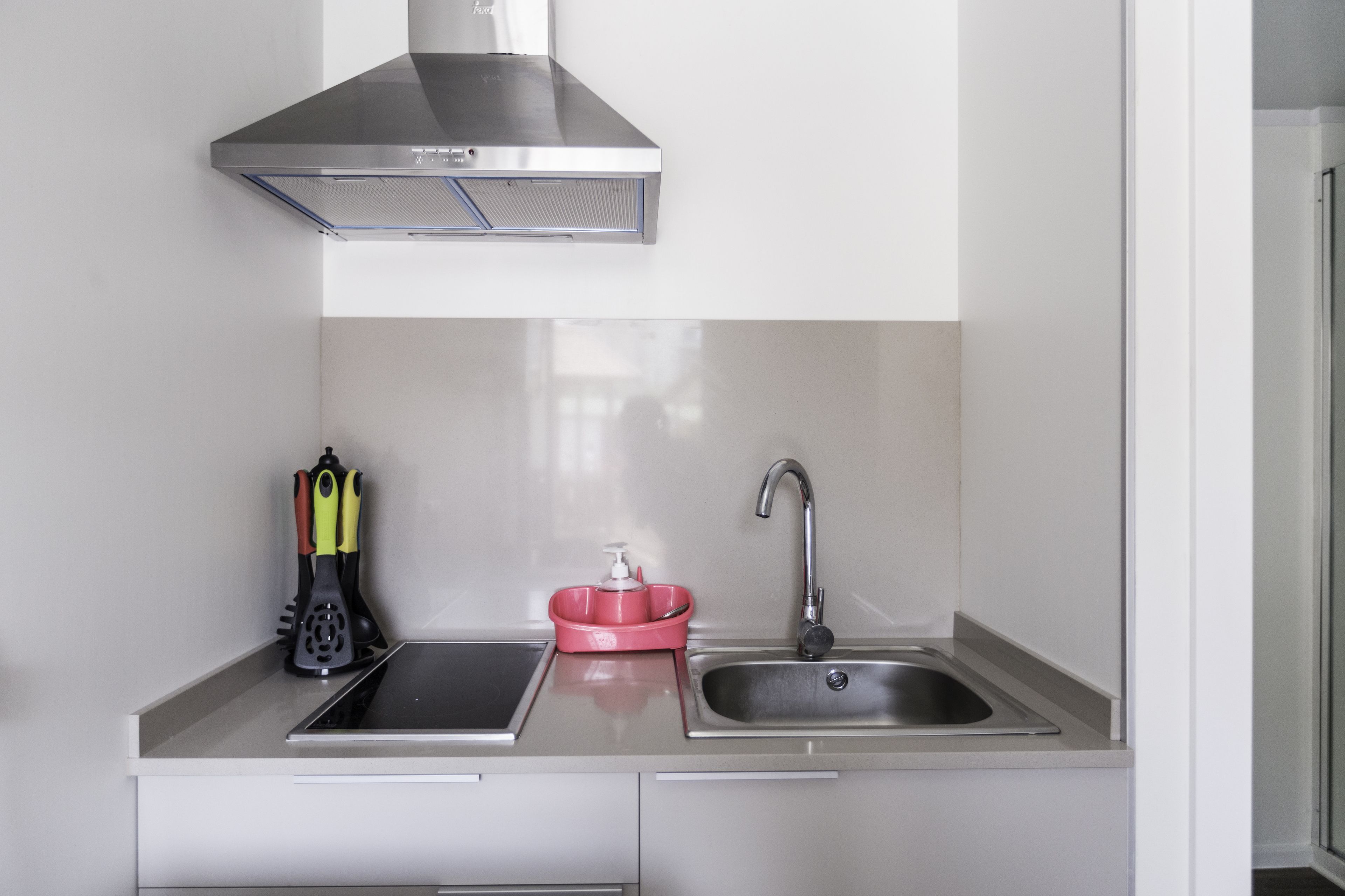 Una cocina con campana extractora de acero inoxidable, un fregadero y una encimera con un jabonera roja y utensilios de cocina.