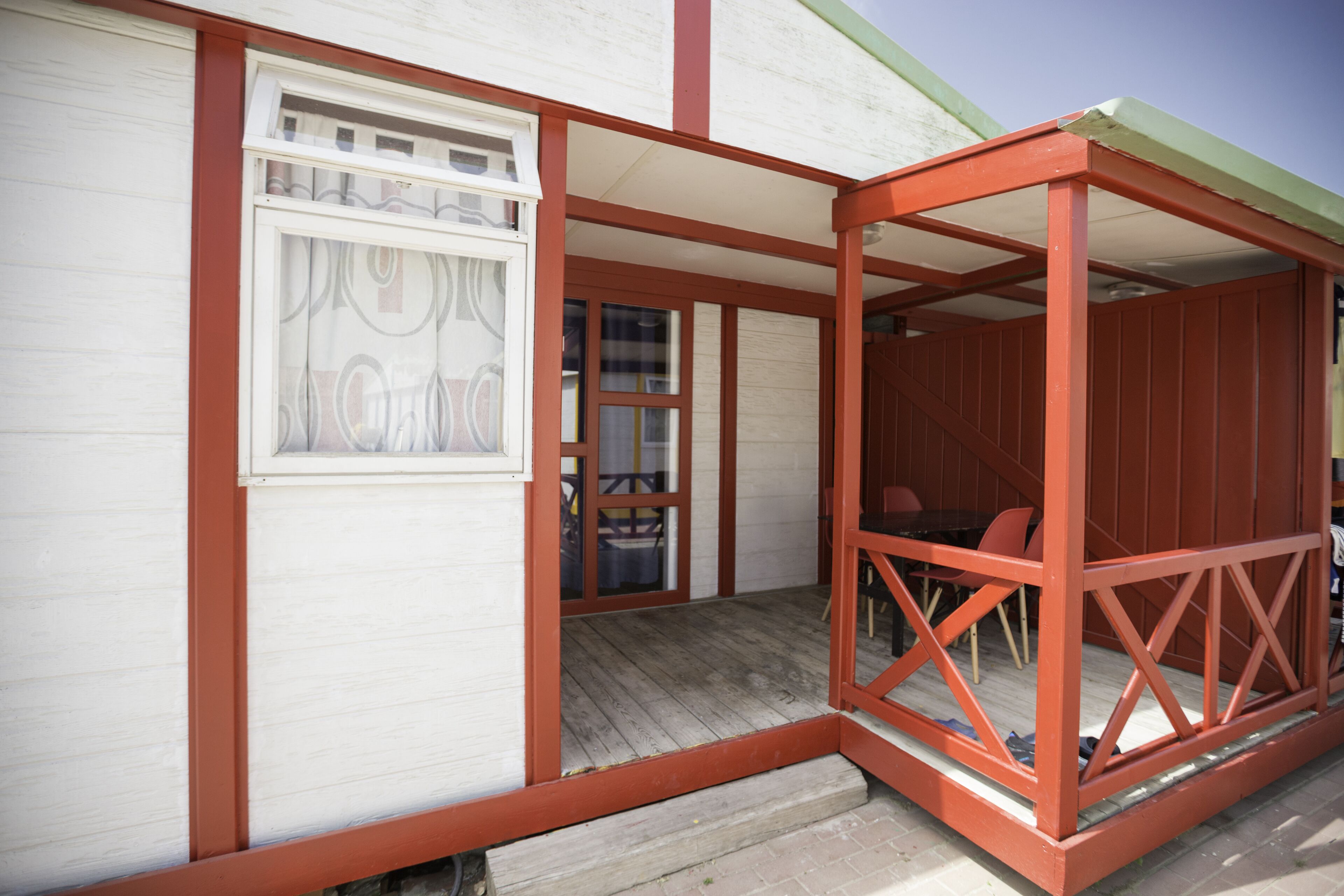 Un área de estar al aire libre cubierta con piso de madera y estructura roja.