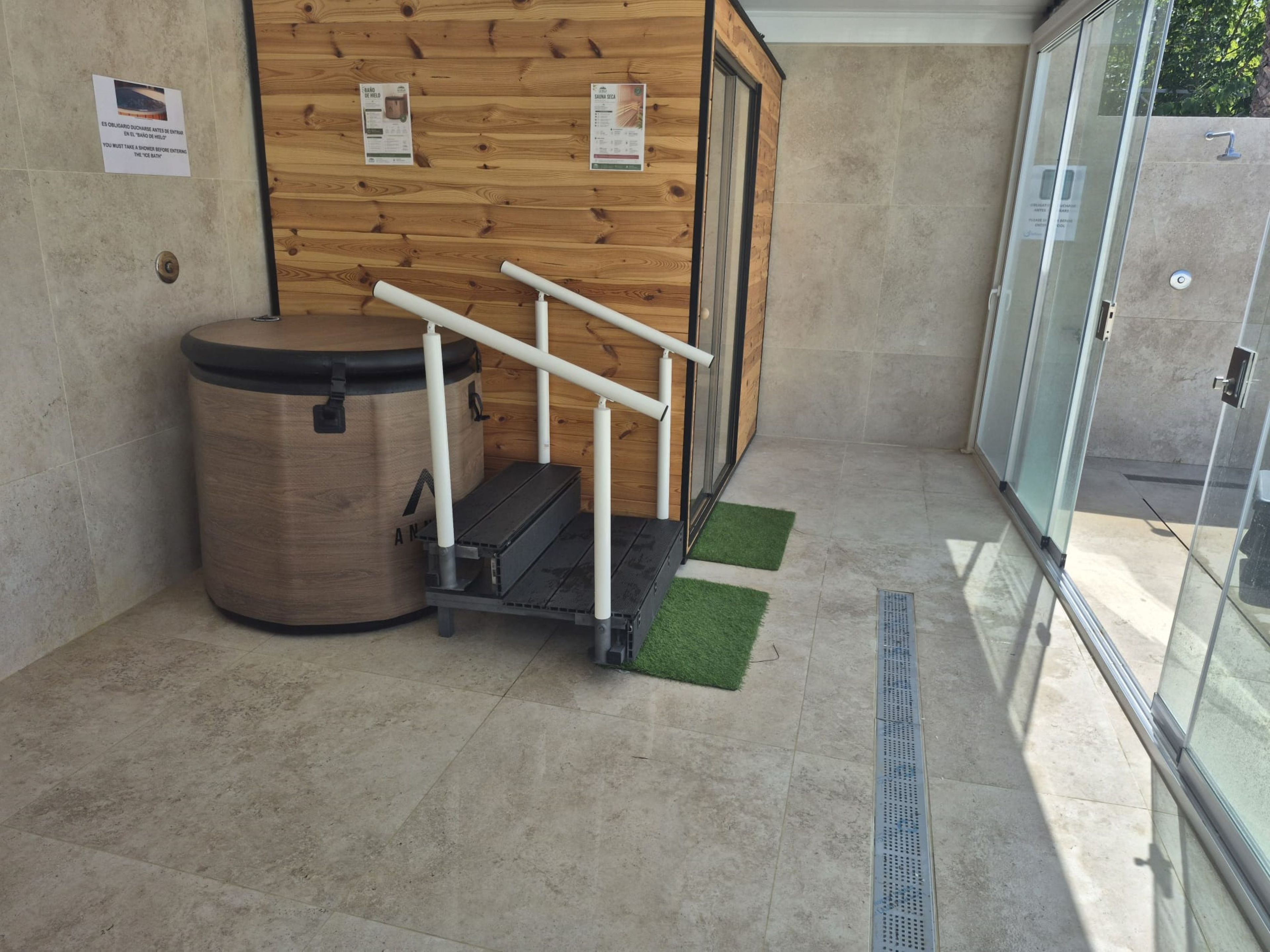 A modern bathroom with a wooden wall, a trash bin, a shower area, and a glass door leading outside.