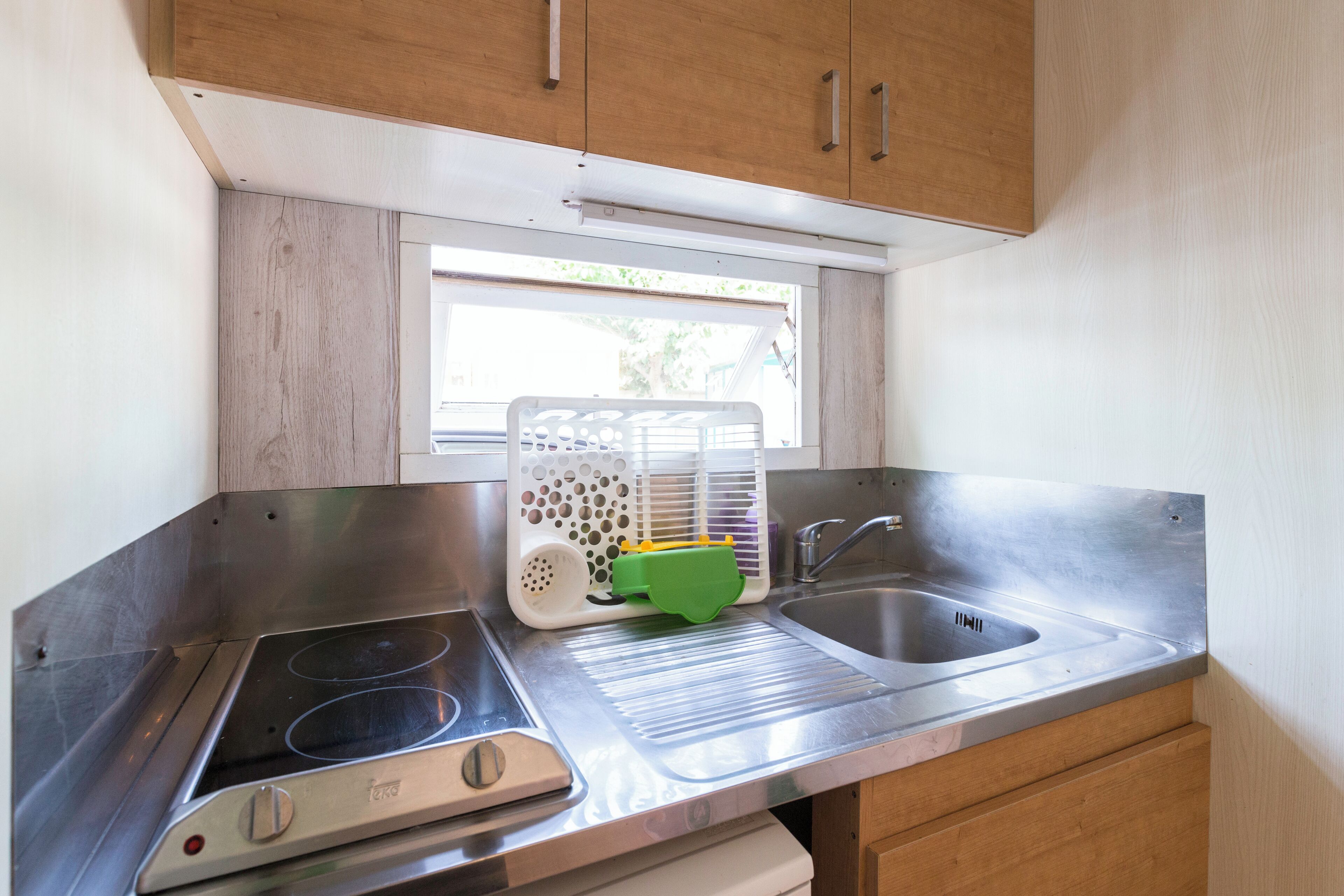 Una cocina compacta con un lavamanos de acero inoxidable, una estufa integrada y armarios de madera.