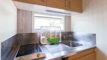 Una cocina compacta con un lavamanos de acero inoxidable, una estufa integrada y armarios de madera.