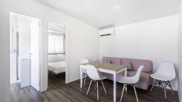 Habitació moderna i minimalista amb taula de dinar de fusta, cadires blanques, sofà rosa i llit blanc.