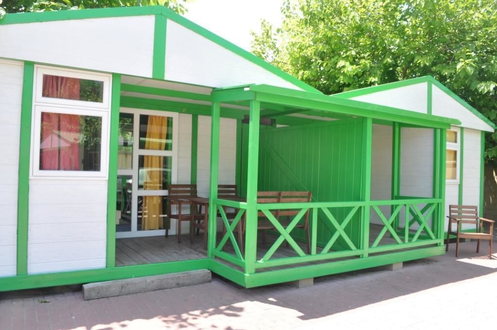 A small, single-story building with a green exterior and white trim, featuring a covered porch with wooden benches.