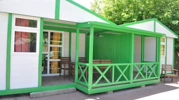 A small, single-story building with a green exterior and white trim, featuring a covered porch with wooden benches.